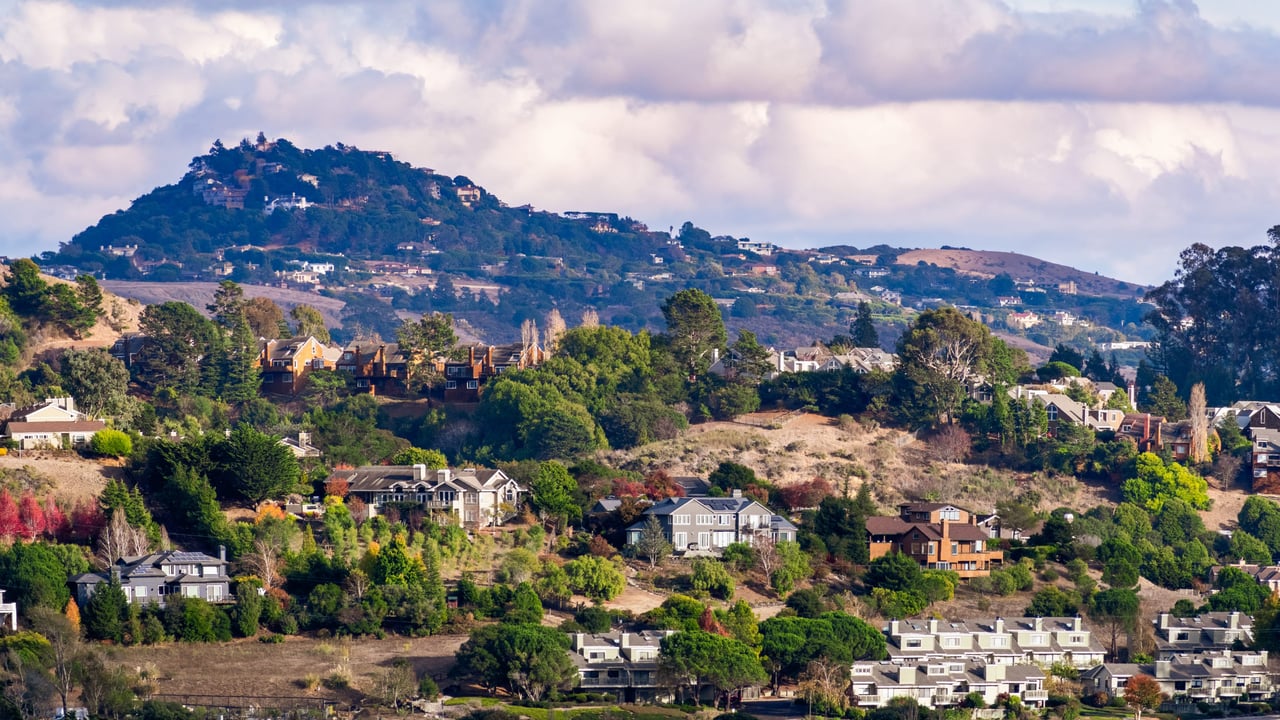 A group of houses with colorful roofs sit on a hilltop.