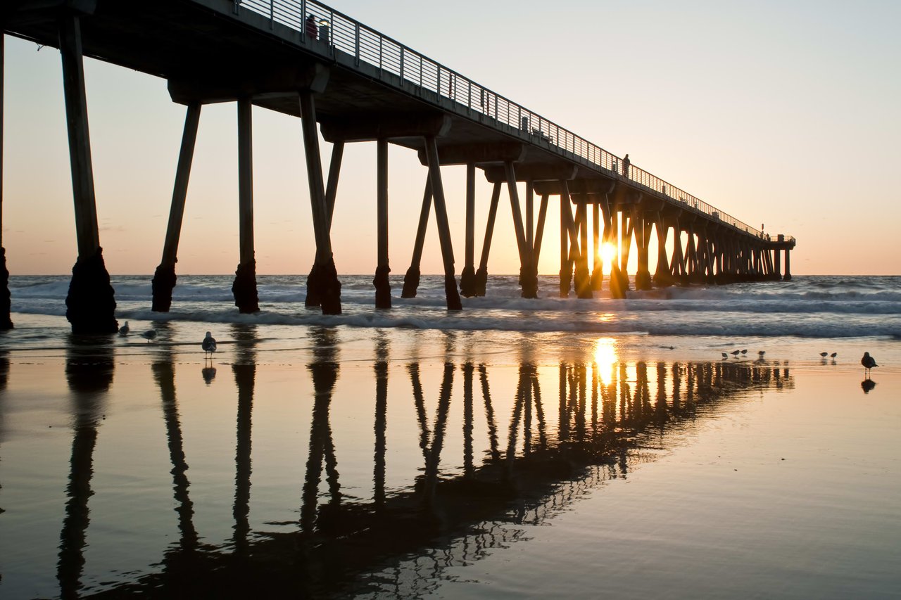 A long pier stretches into a calm ocean, bathed in the warm glow of a vibrant sunset.