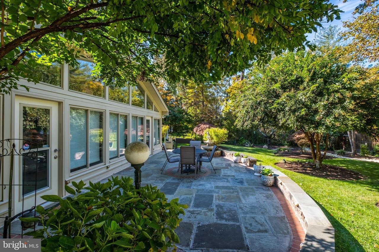 Home with a spacious stone patio, outdoor dining set, and leafy landscaped yard.