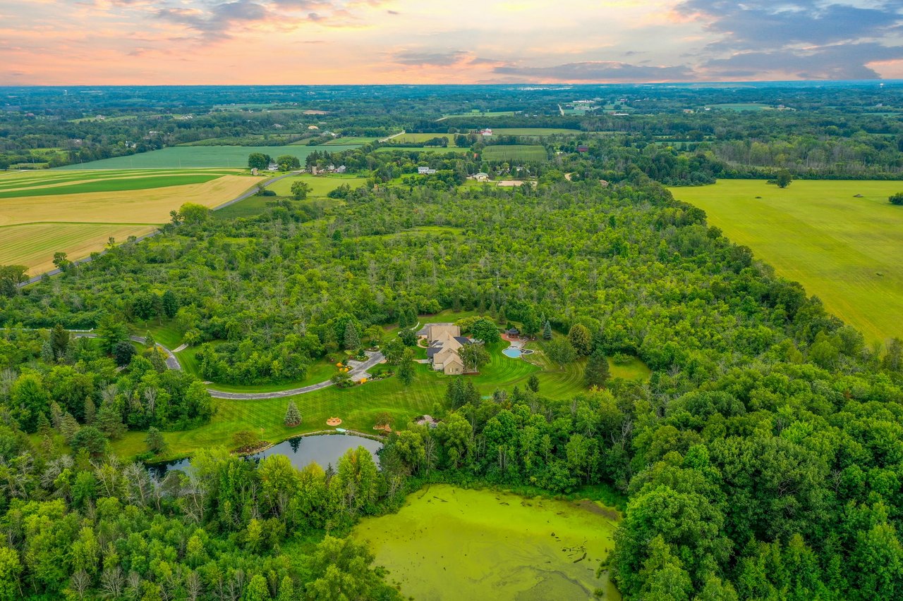 Mequon, WI aerial shot of a large property with greenery, pool, and pond at sunset.