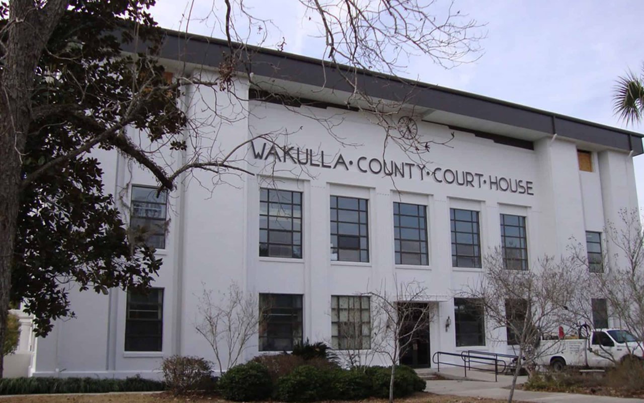 A historic courthouse building with a sign reading "Wakulla County Courthouse." The building is surrounded by trees and has a traditional architectural style.