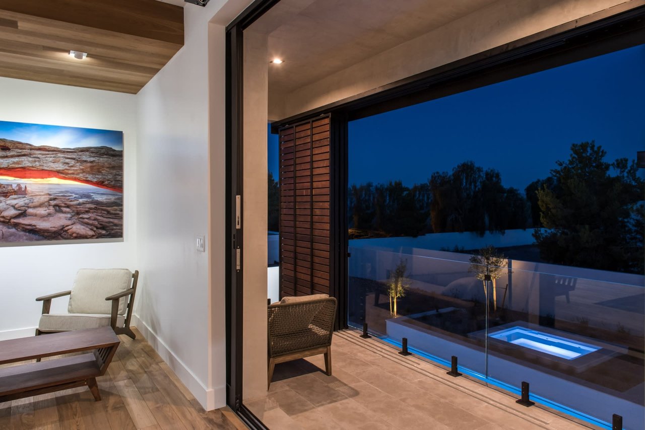 Modern sitting area opening onto a balcony overlooking an illuminated pool at night.