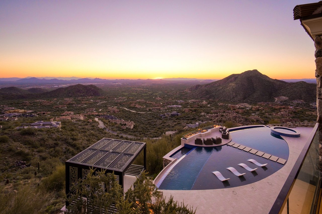 Infinity pool overlooking a sprawling valley with a sunset backdrop.