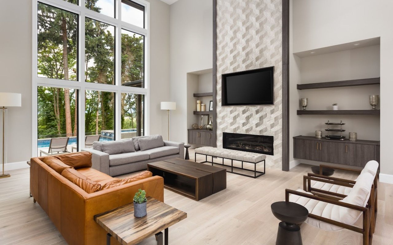 A modern living room with floor-to-ceiling windows, a fireplace, a leather sofa, a TV, and neutral decor.