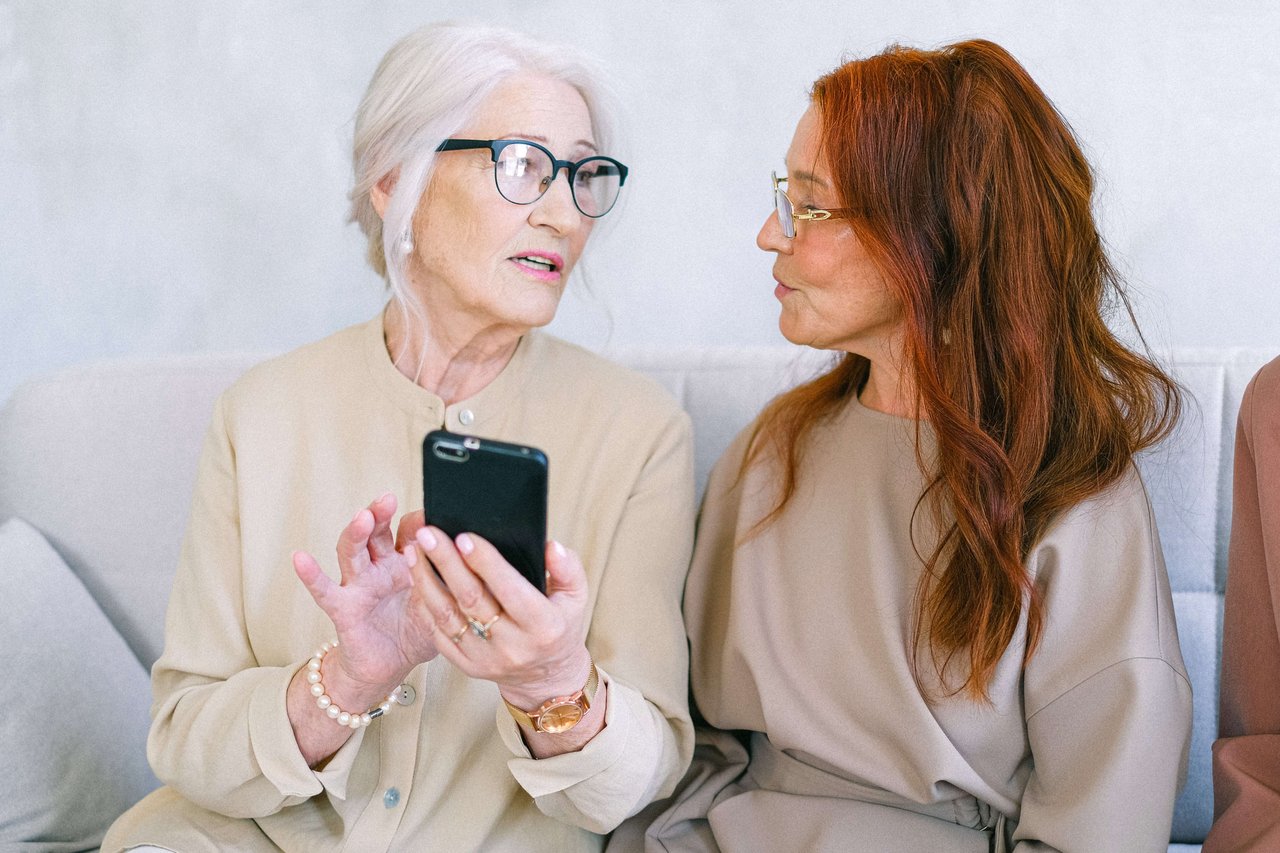 an older woman with phone on hand talking to another older woman