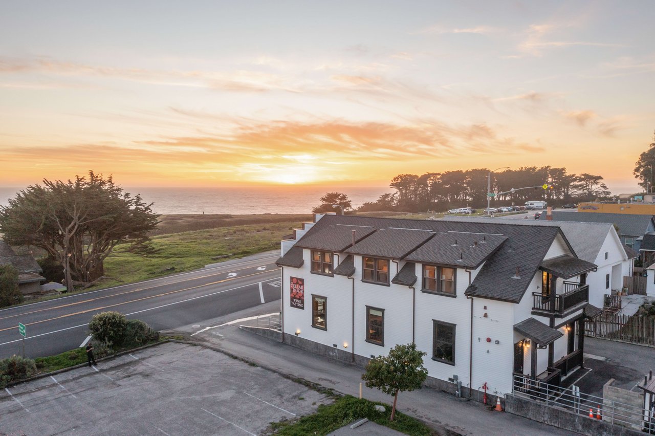 White coastal building beside a road, with ocean and sunset behind it.