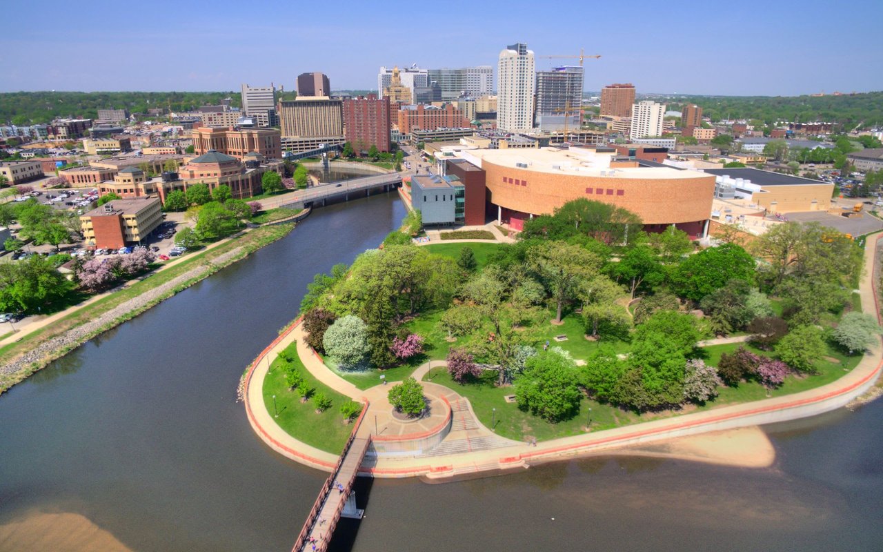 An aerial view of a city with a winding river and a suspension bridge in the foreground. 