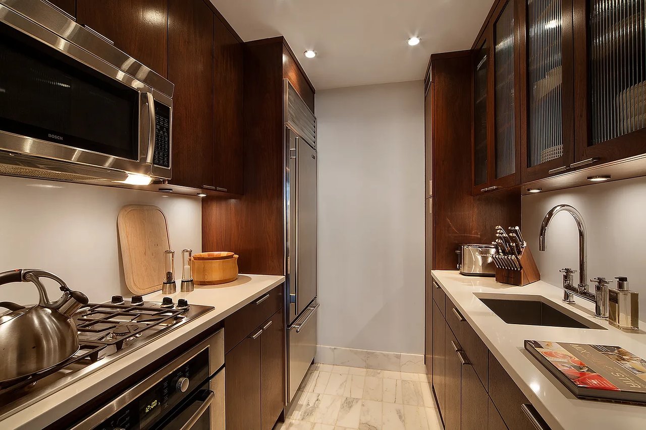 Galley kitchen with dark wood cabinets, stainless steel appliances, and white marble flooring.