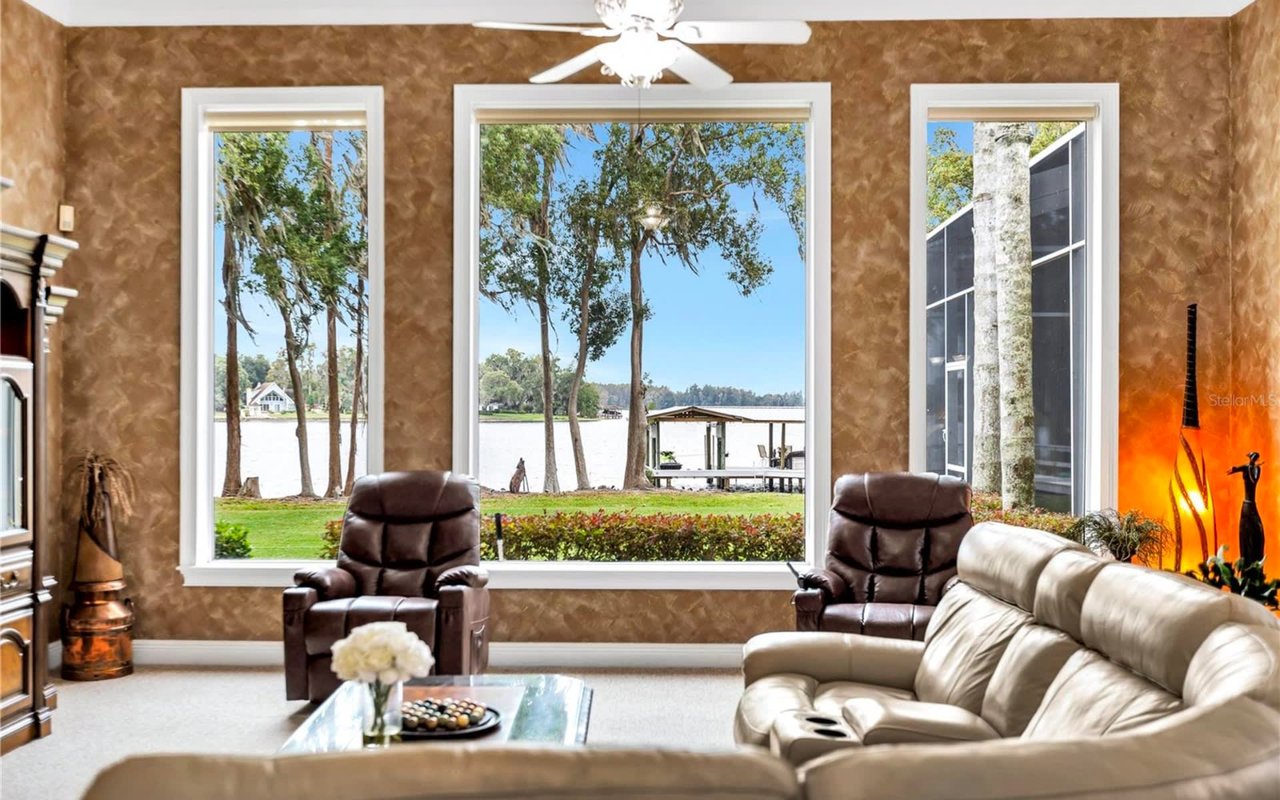 A rustic living room with a lake view furnished with a couch, a coffee table, two armchairs, and a fireplace.