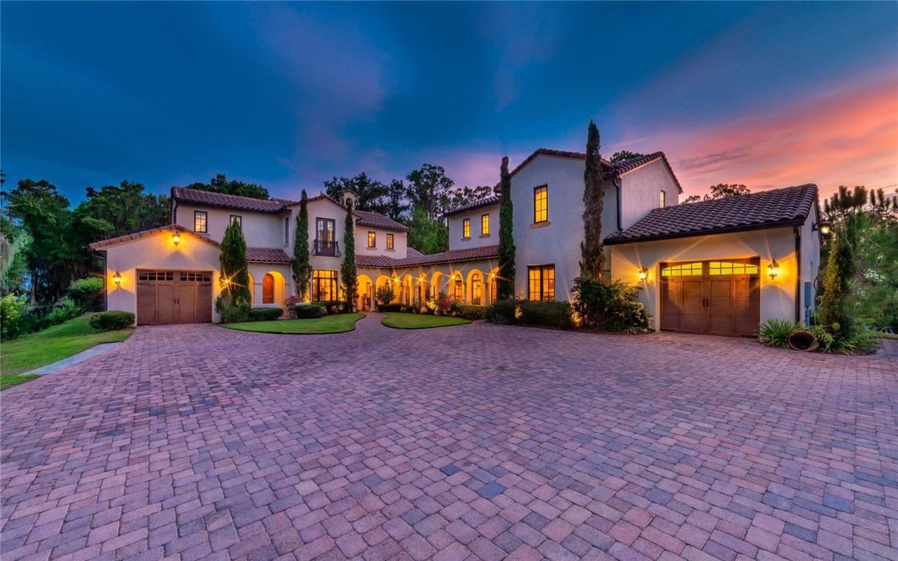 A two-story house with a brick driveway, two garages, and a curved sidewalk lined with trees and green lawns in Golden Oak.