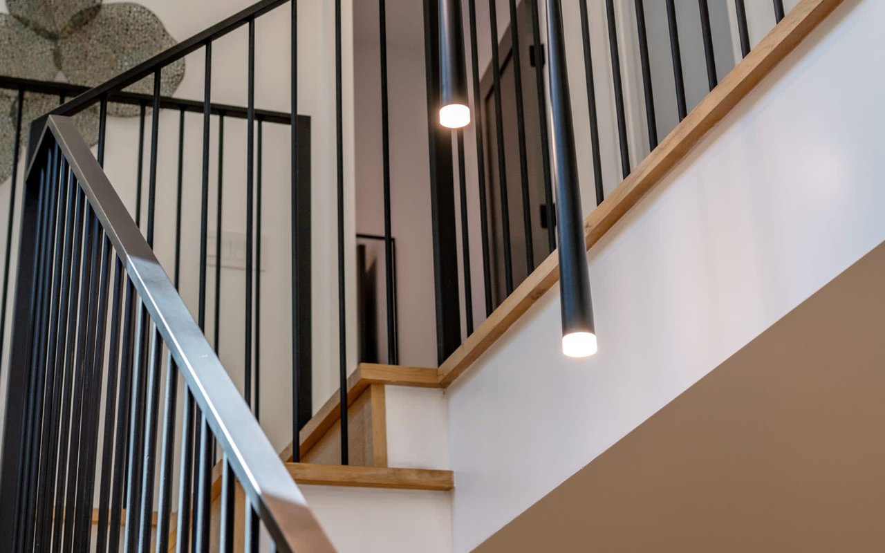 Interior staircase with black metal railings, light wood steps, and pendant lights.