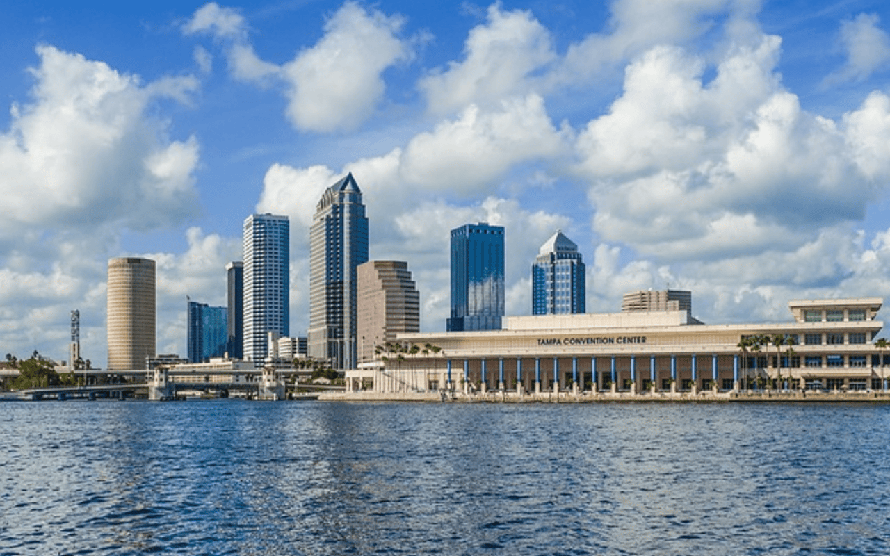 A cluster of modern skyscrapers of varying heights and designs rise into a bright blue sky 