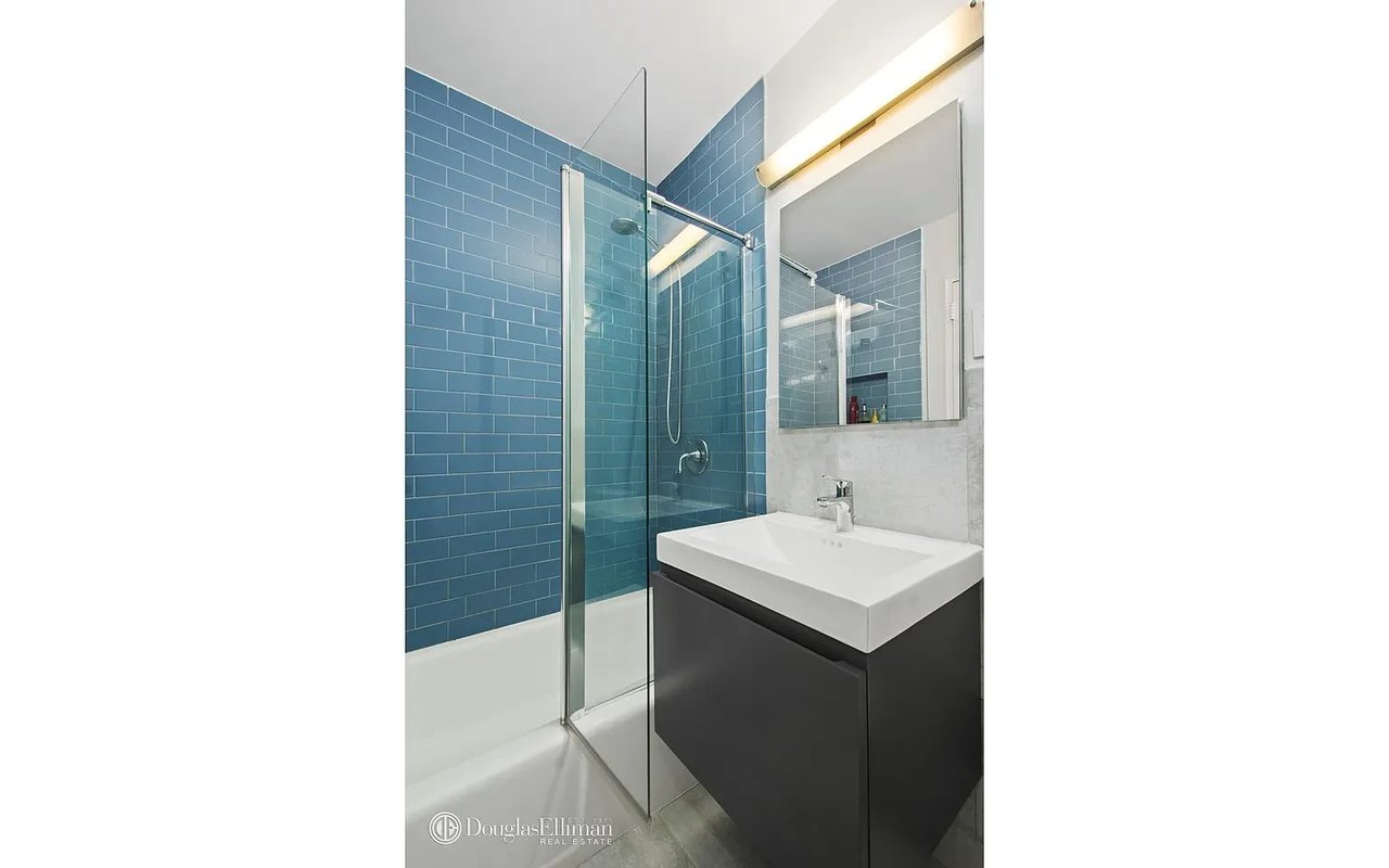 Bathroom with blue subway-tile shower walls, a glass enclosure, and a white sink on a dark vanity.