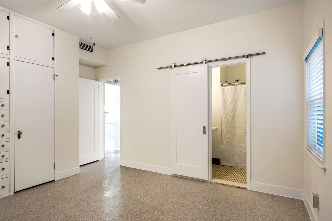 A view of the interior room of a house with light walls and ceiling. The floor is made of speckled and polished material. There are built-in cabinets and drawers providing ample storage space.