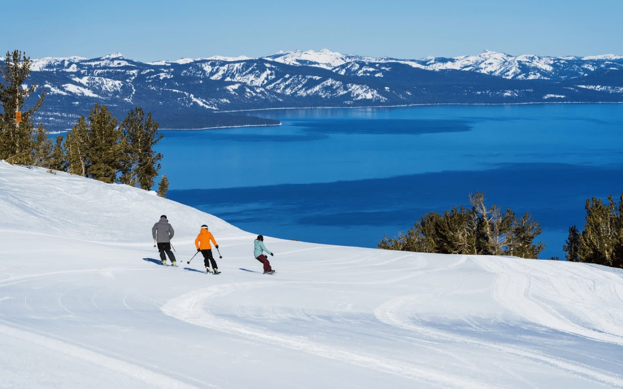 Skiers enjoying a winter adventure on a snowy mountain, surrounded by views of trees, a lake, and distant mountains.