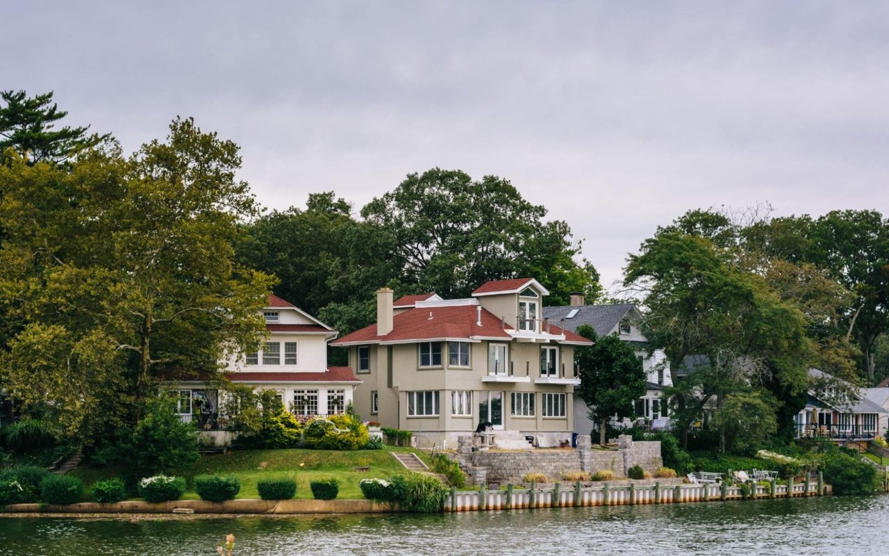 A large house with a red roof sits on a hill overlooking a lake.