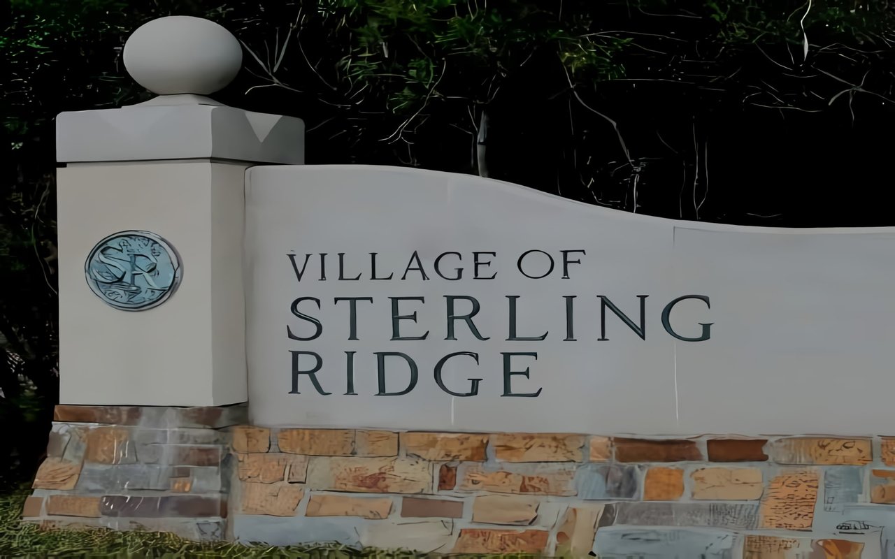 The sign has a light-colored, wavy upper portion with the text, and a base constructed of multi-toned brown and grey stacked stone or brick. 