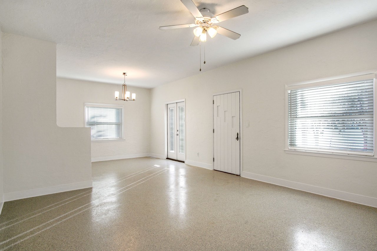 Another view of the main living area, showcasing its spaciousness and natural light from large windows. The room includes a ceiling fan and tiled floors.