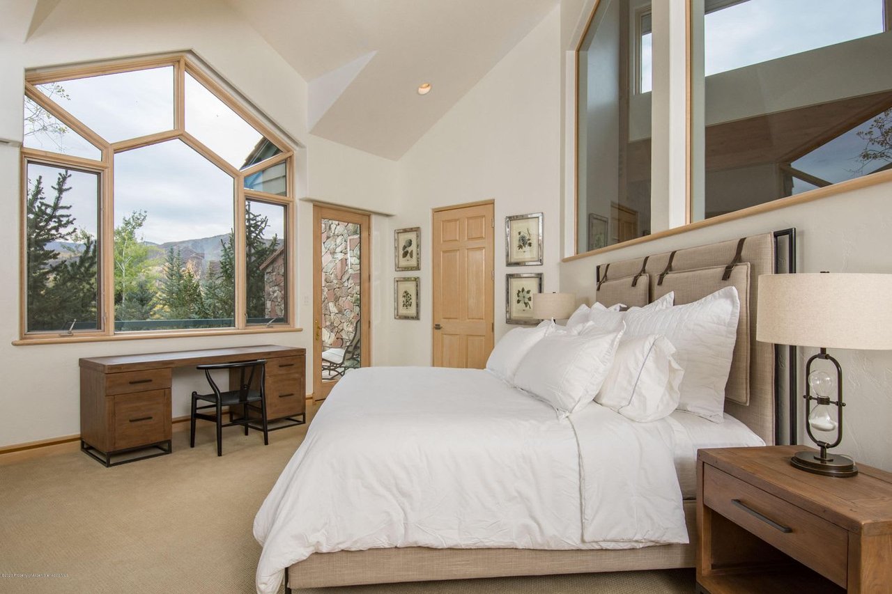 Bedroom with a white bed and tall windows overlooking mountains.
