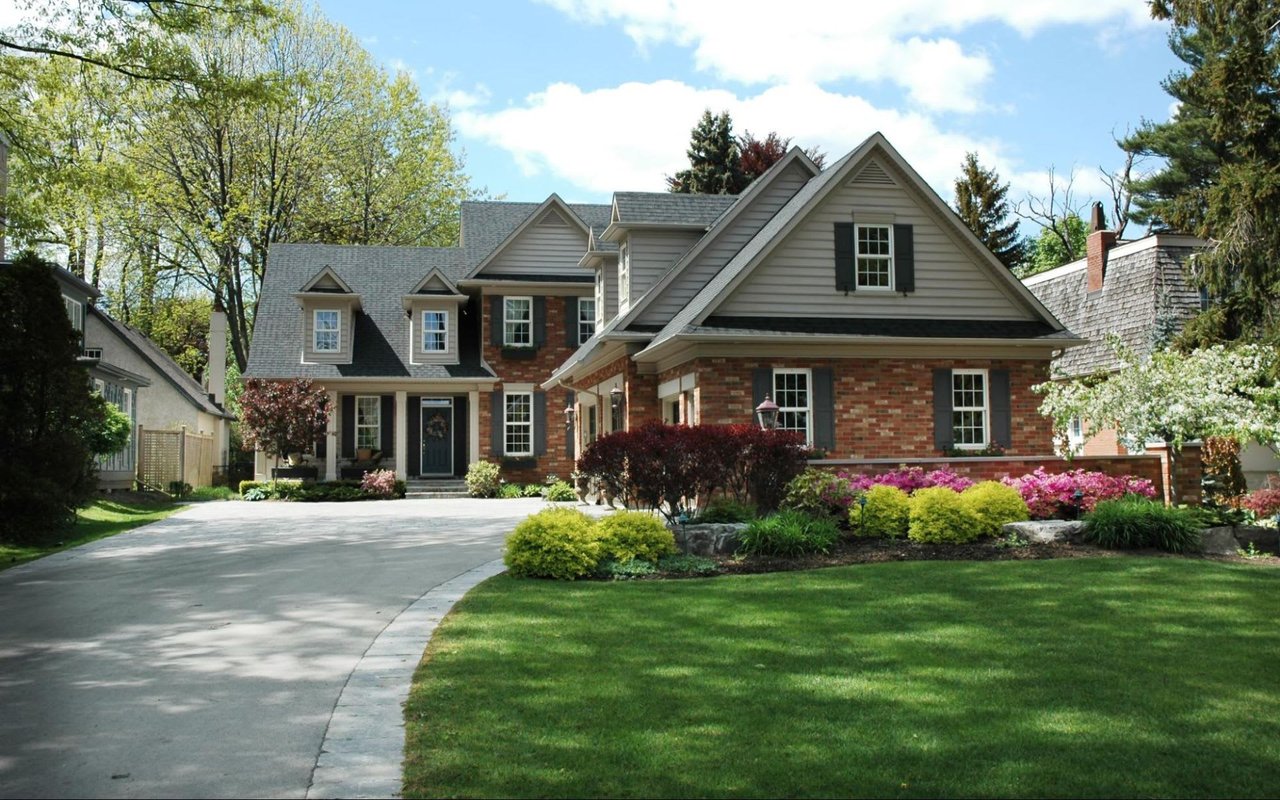 Two-story white house in a quiet suburb, with red brick exterior, gray slate roof, lush green front lawn, and 2-car garage.