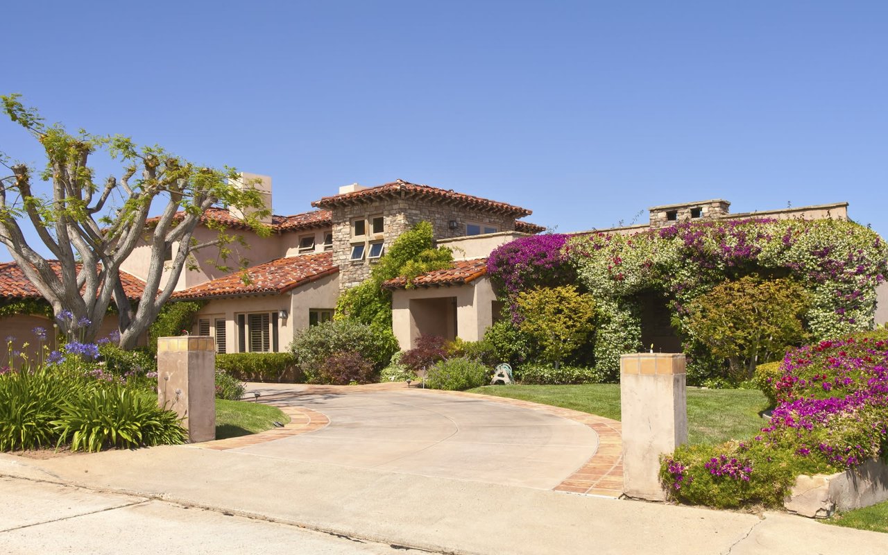 A large house with a driveway leading to it, and flowers in front