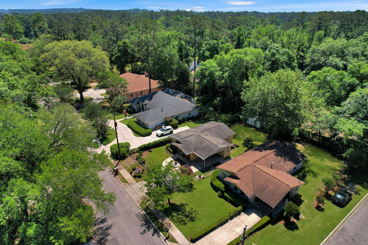 An aerial view of houses in Tuskegee showing rooftops and yards. The area is heavily wooded with trees surrounding the homes.