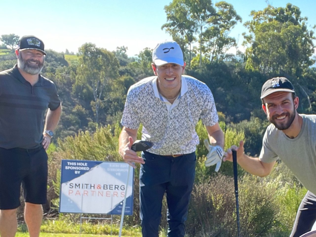  Three men are standing on a golf course under a clear sky. 