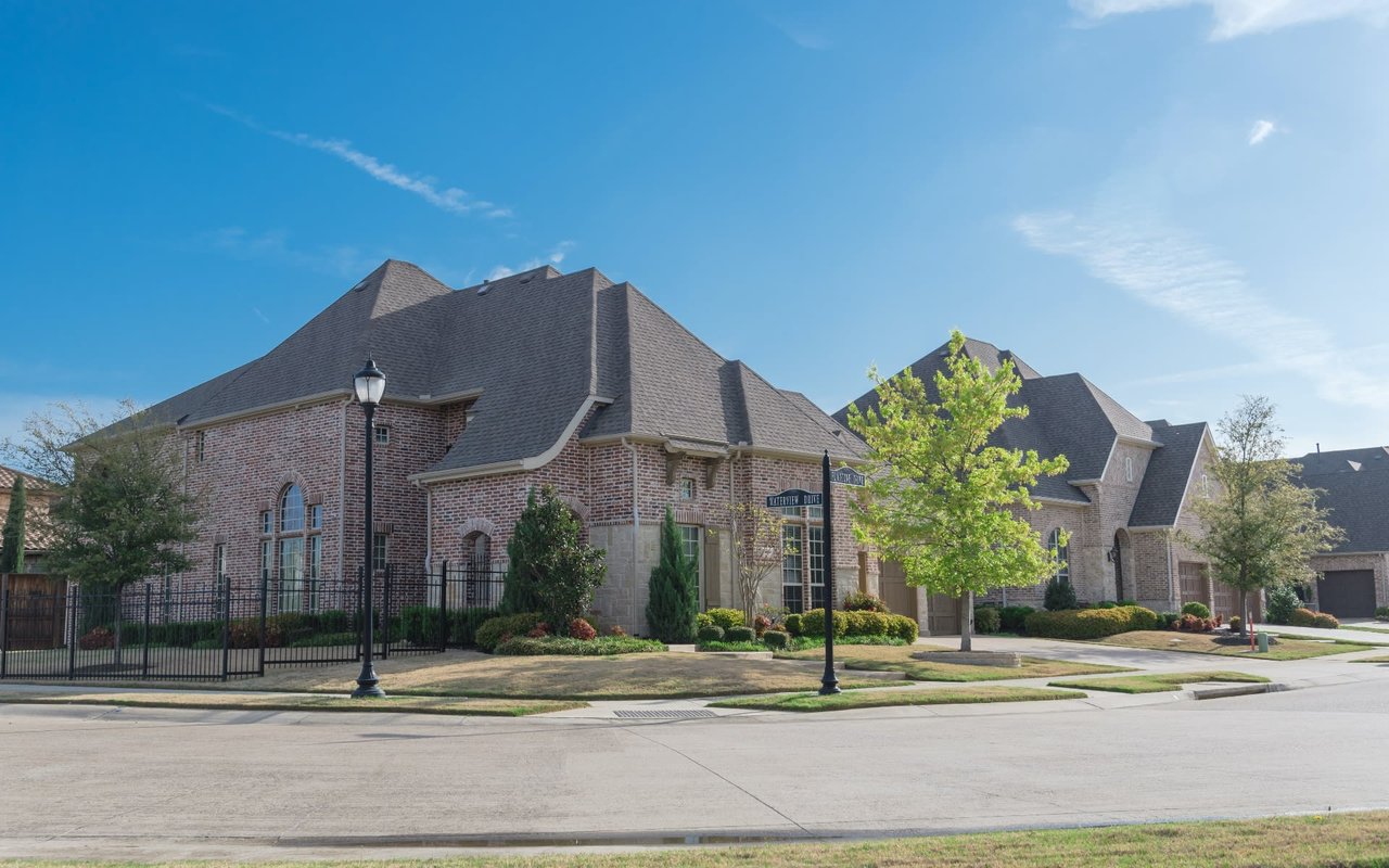 A row of large, two-story brick houses with black slate roofs, attached car garages, pathways, and front lawns.