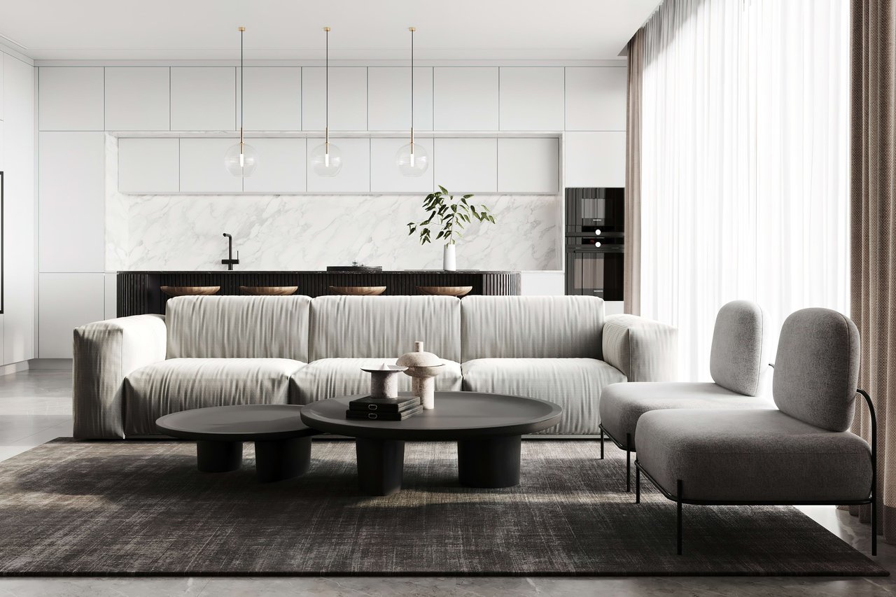 Modern living room with a pale sofa, gray chairs, black coffee tables, and an open marble-backed kitchen.
