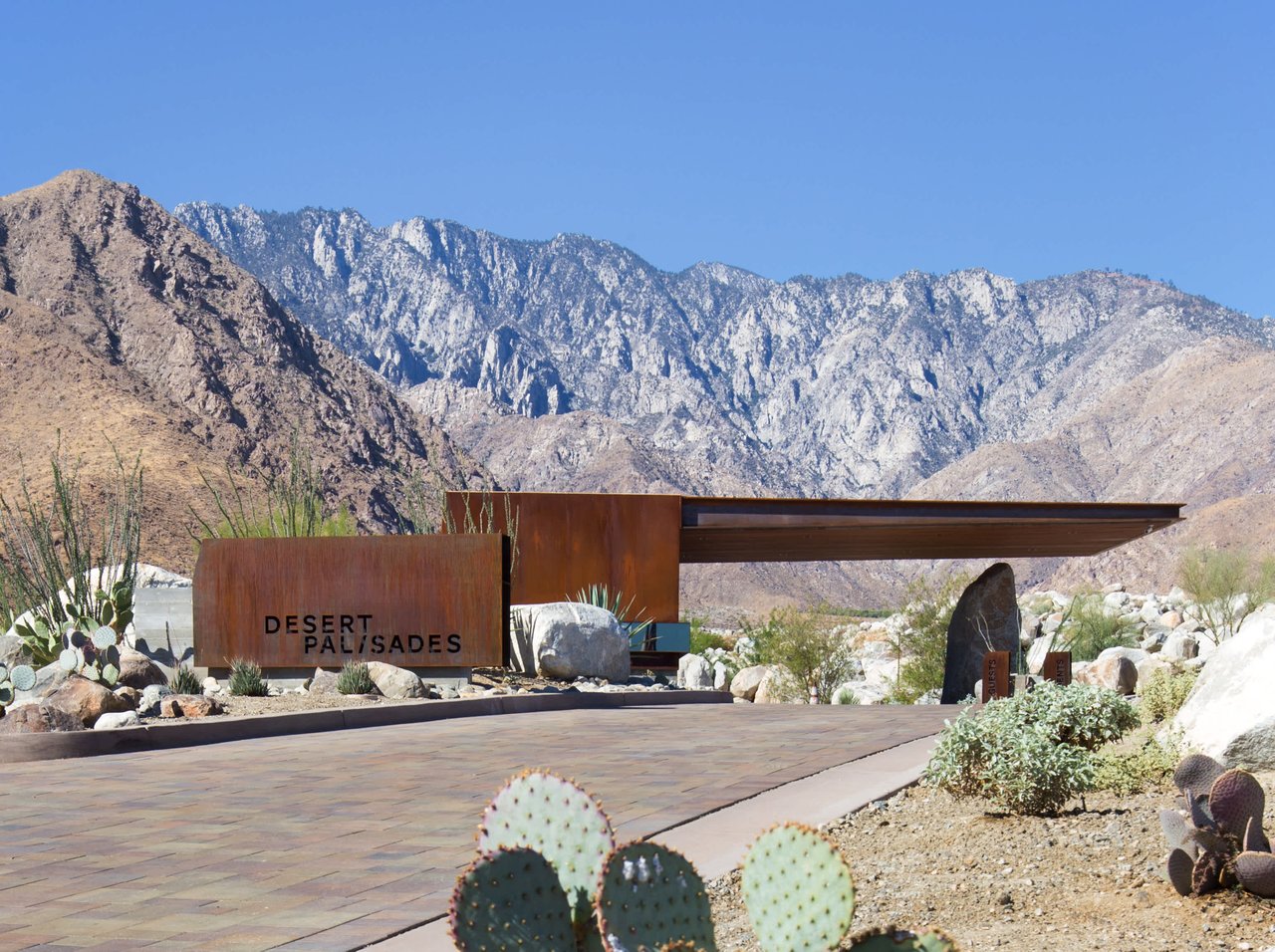 Desert Palisades entrance sign and canopy framed by desert landscaping and rugged mountains.