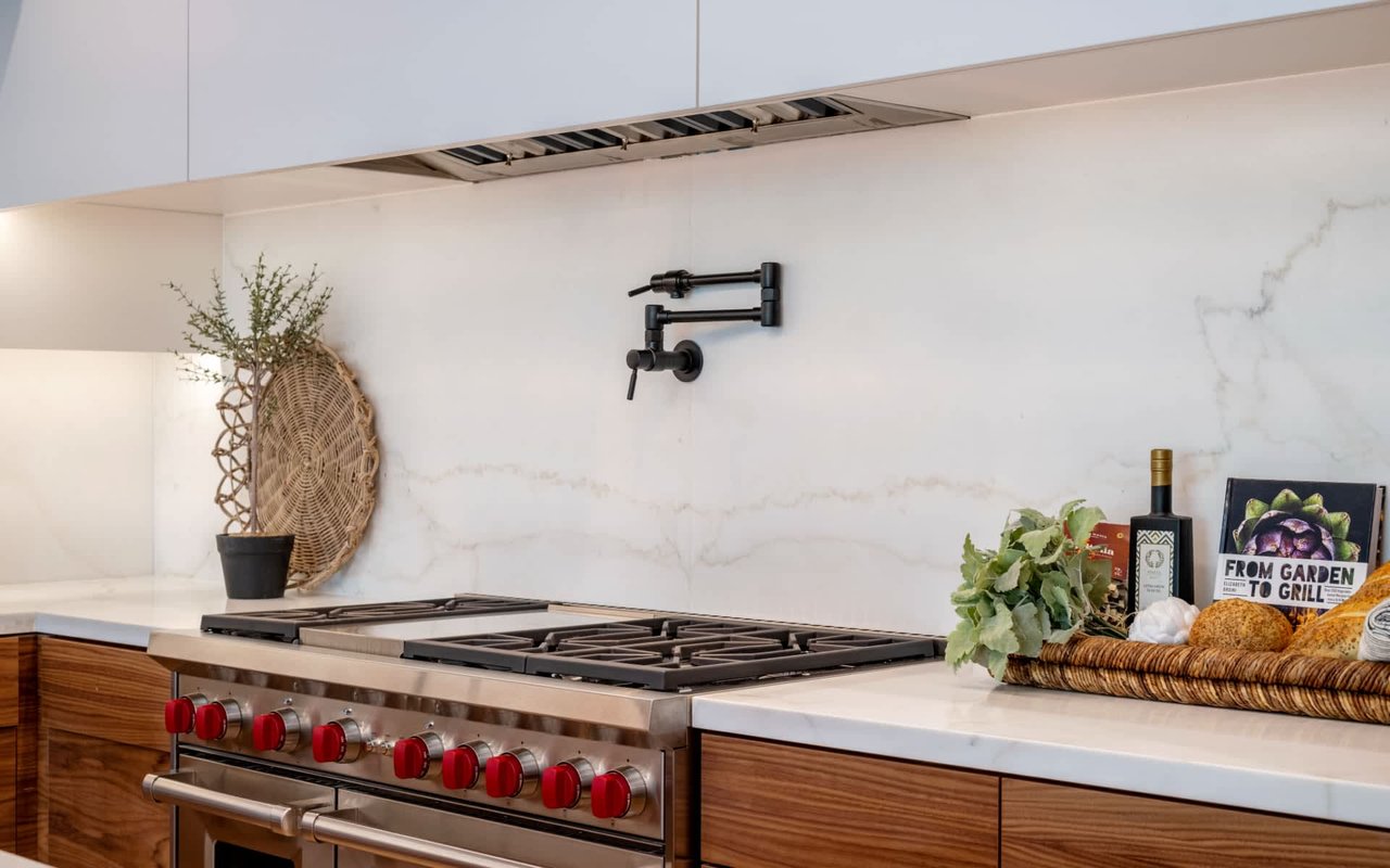 Staged kitchen with a stainless-steel gas range, red knobs, marble backsplash, and warm wood cabinetry.