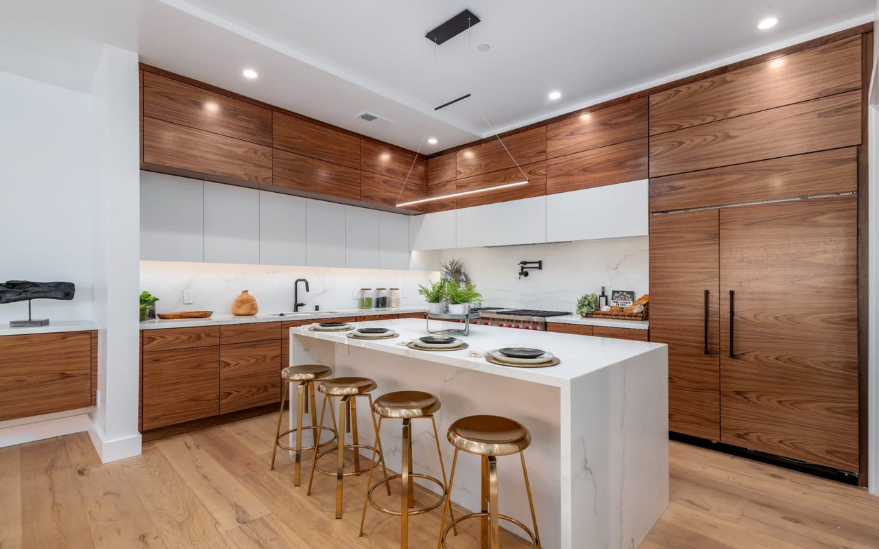 Modern kitchen with walnut cabinetry, a white island, and brass stools.