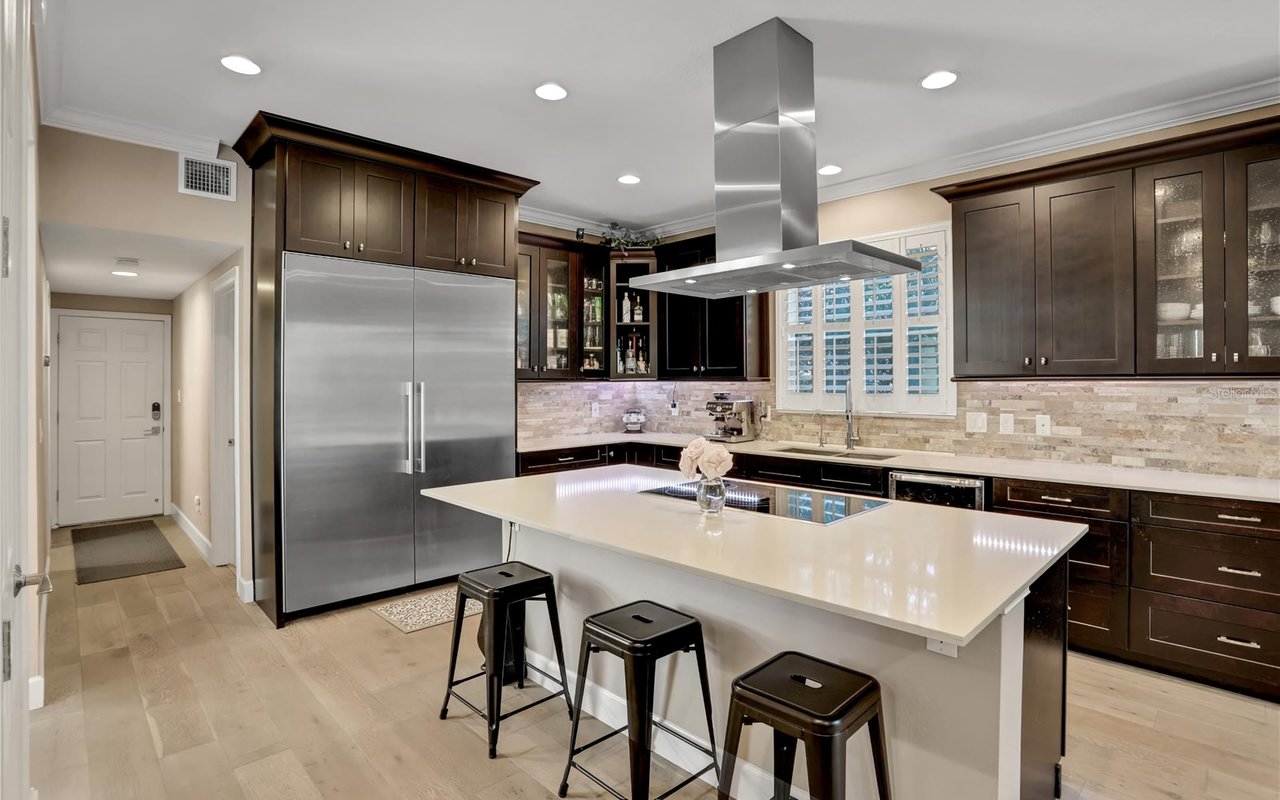 A kitchen with stainless steel appliances, a large center island with pendant lights, cabinets, and a window above the sink.