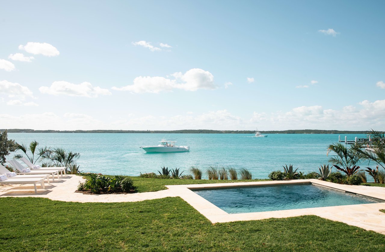  A tranquil coastal scene features a rectangular swimming pool with light-colored coping in the foreground, set into a well-maintained green lawn.