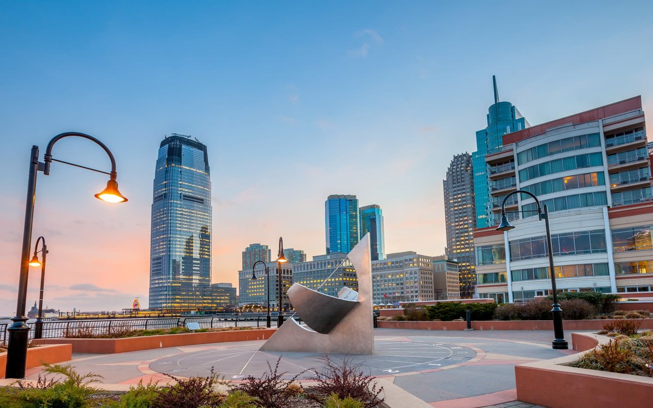 The Jersey City skyline at sunset, with tall skyscrapers and modern buildings.