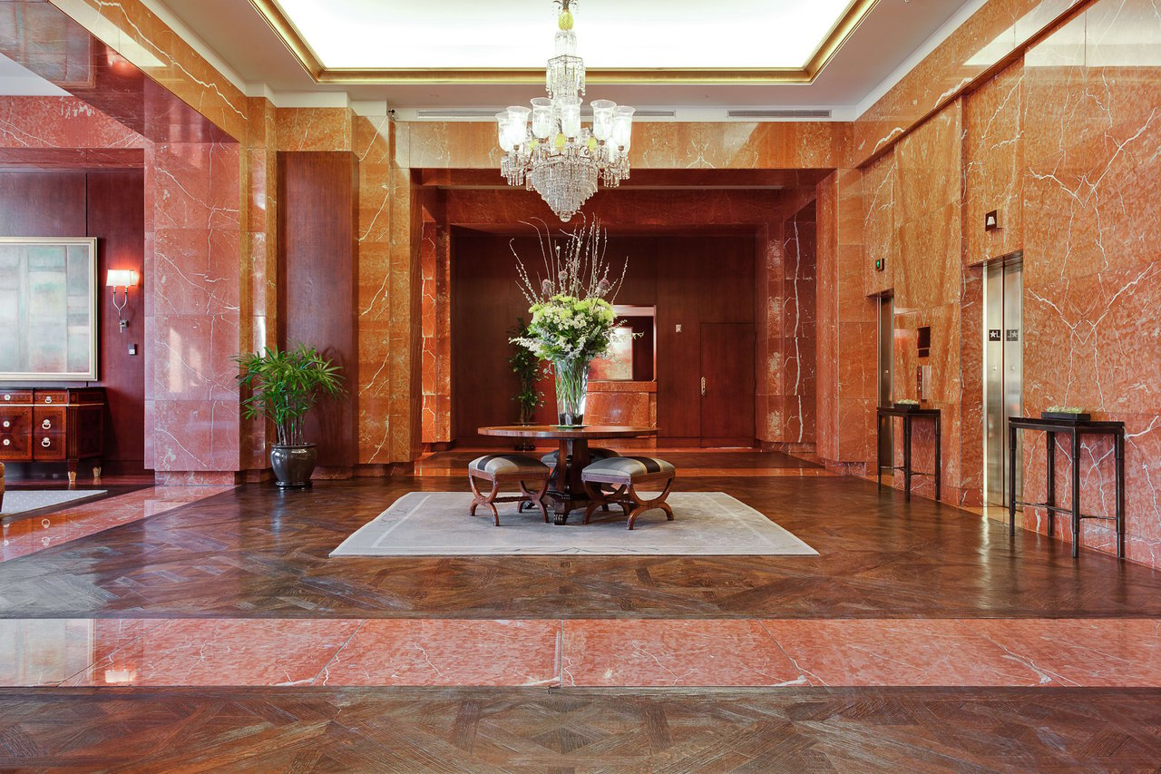 A lavish lobby greets guests with grandeur, showcasing a marble floor, cascading chandelier, and opulent floral arrangement.