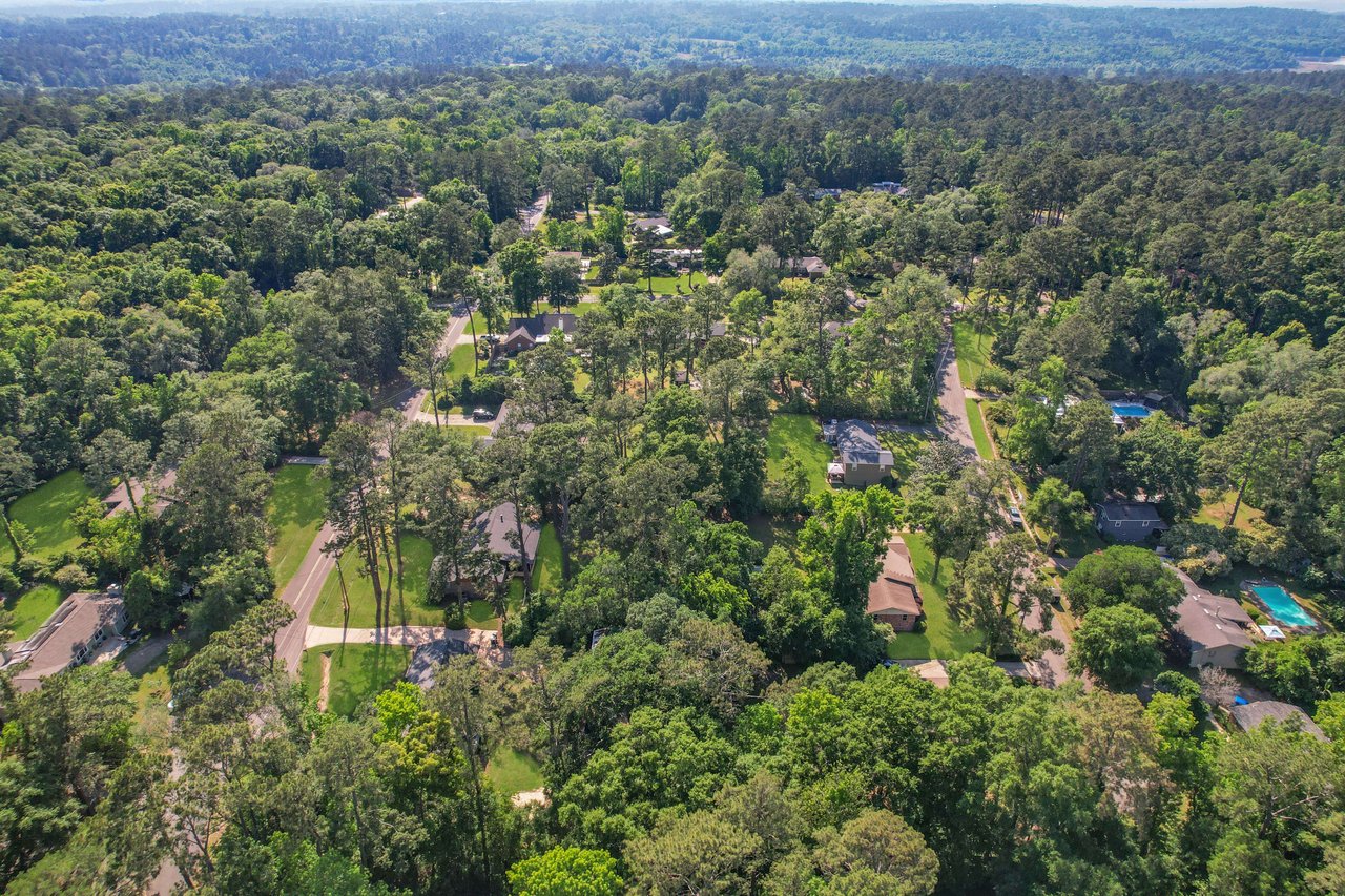 An aerial view of Linene Woods, highlighting the layout of houses within a dense forested area. The homes are well-spaced and surrounded by nature.