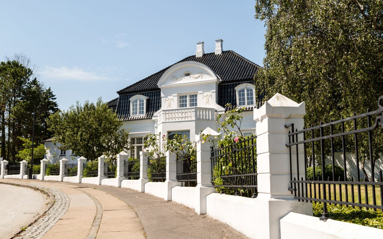 gated white luxury home on Side of street with blue sky