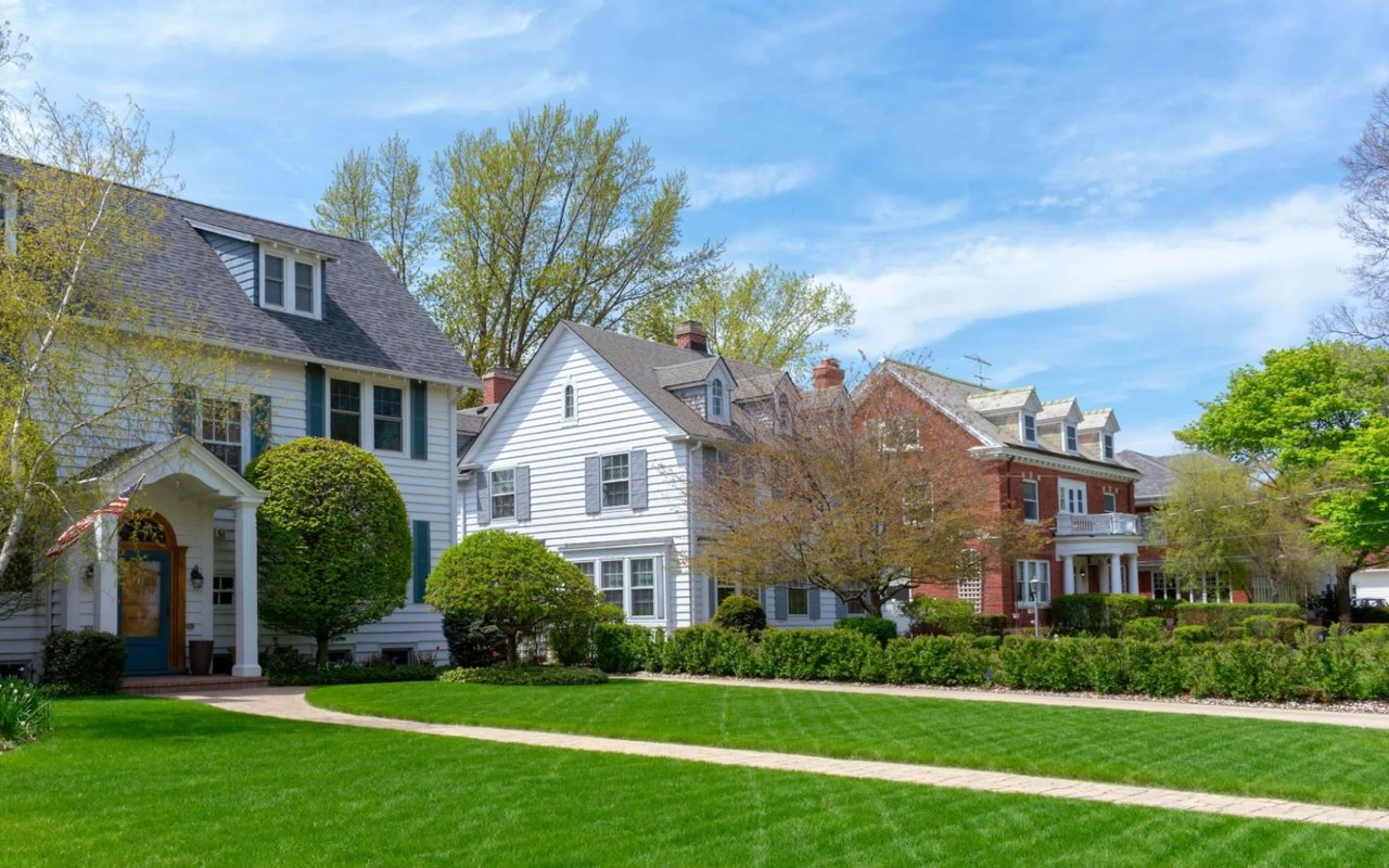 A row of colorful, two-story residential houses with diverse styles, porches, and various landscaping in front.