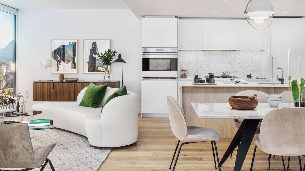 Open-plan kitchen and living area with white cabinetry, a marble dining table, and large windows.