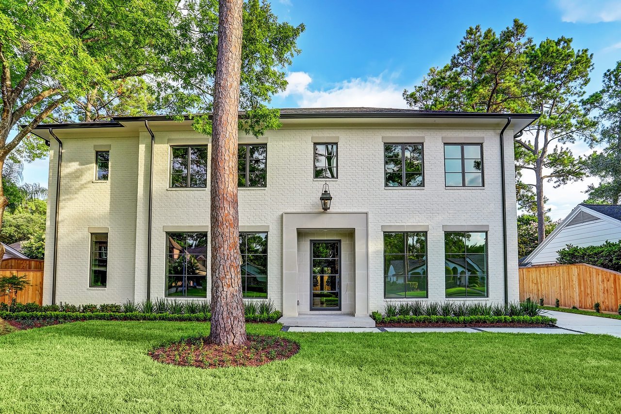 A large white house with a shingled roof, a two-story bay window, a covered porch, an asphalt driveway, and a front lawn.