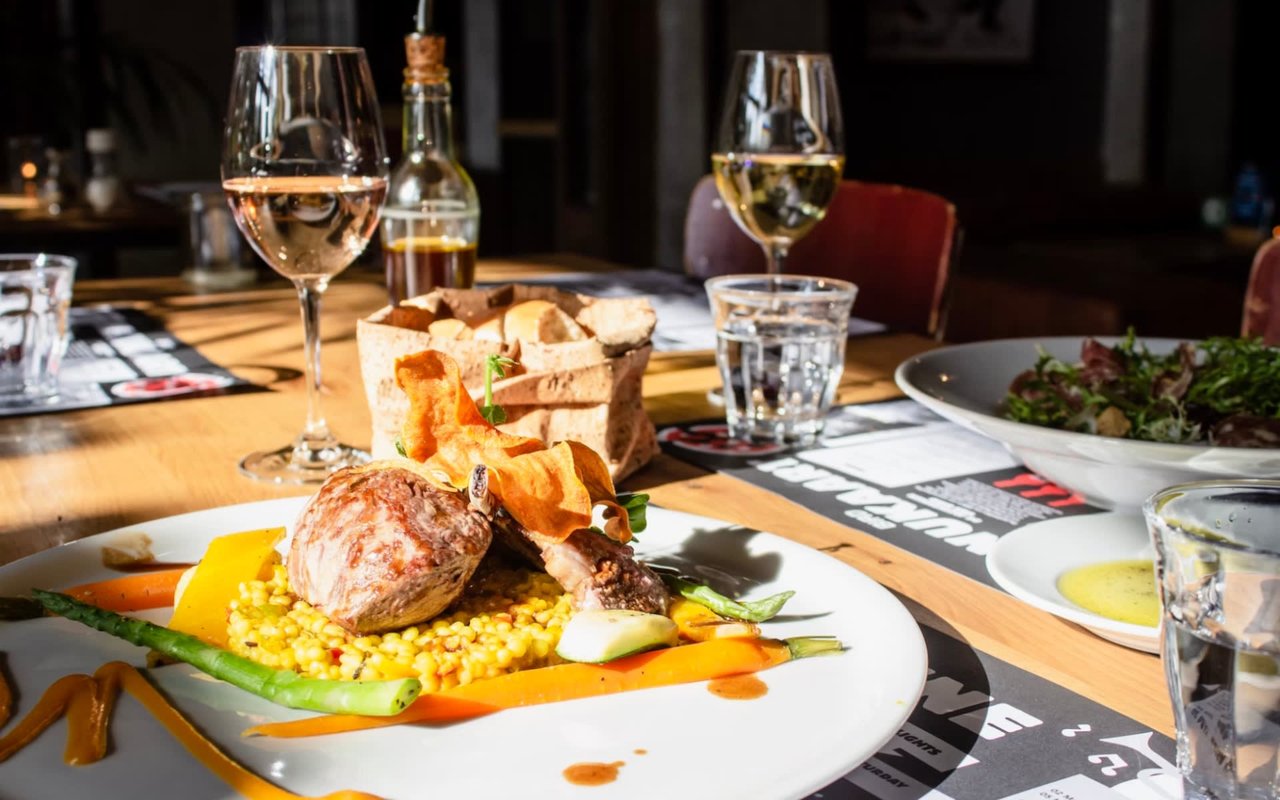 Different savory dishes and glasses of red wine served on a restaurant table.