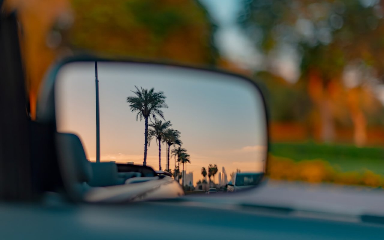 Sideview mirror of car with clear image of pink blue sunset sky and palm trees