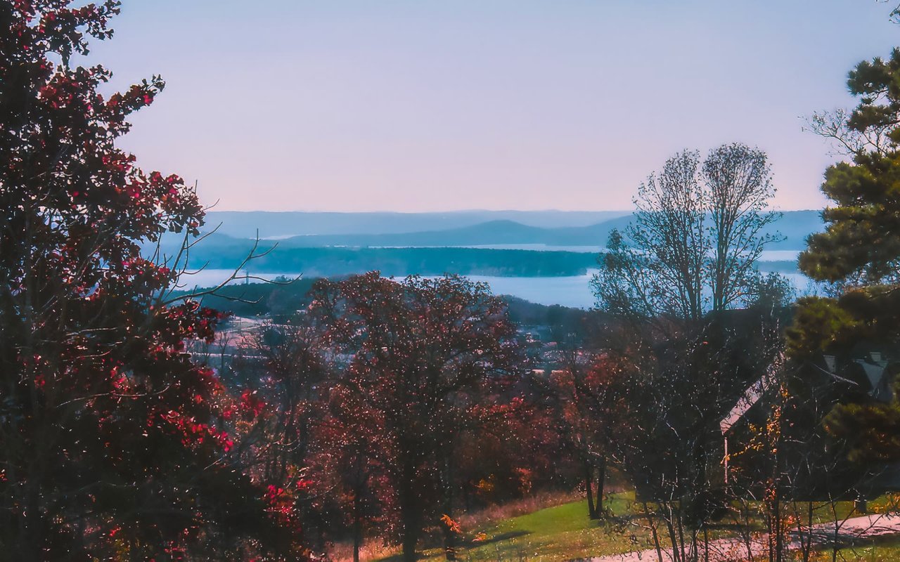 A serene landscape captures a distant lake with hazy blue mountains beyond it,