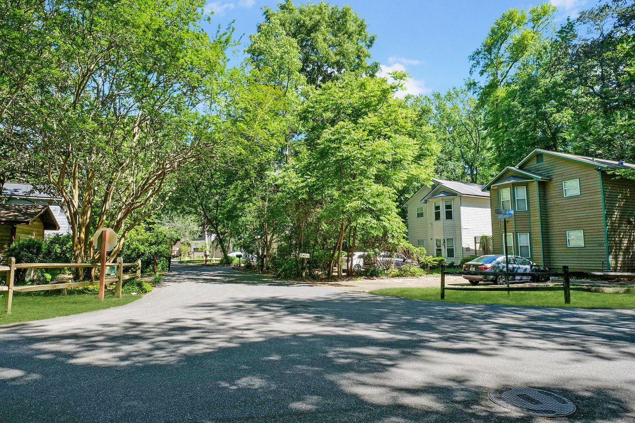 A street-level view within Blairstone Forest, showcasing a residential area with houses, trees, and a shaded road.