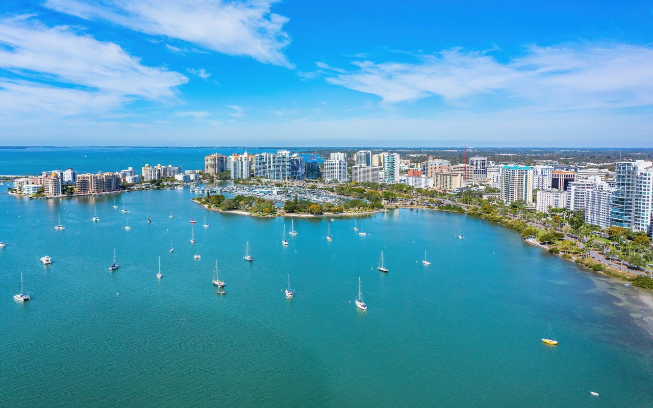 The bay is filled with numerous sailboats and other vessels, and a large marina is visible closer to the city. 
