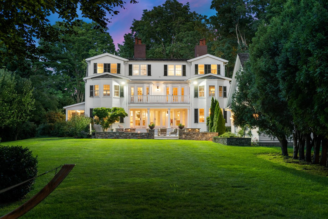  The house features several gables, chimneys, and a spacious porch on the ground floor with a balcony above. 