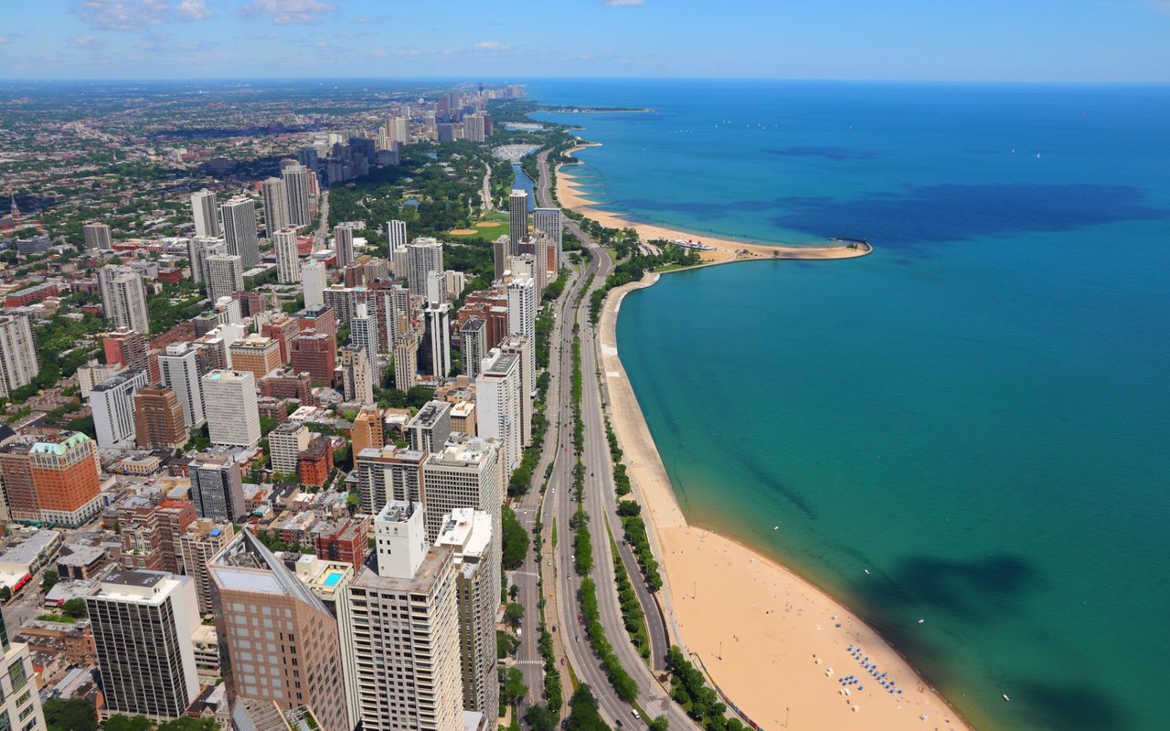 Aerial view of a coastal city with a long pier surrounded by clustered tall buildings in a high-rise area on a beach.