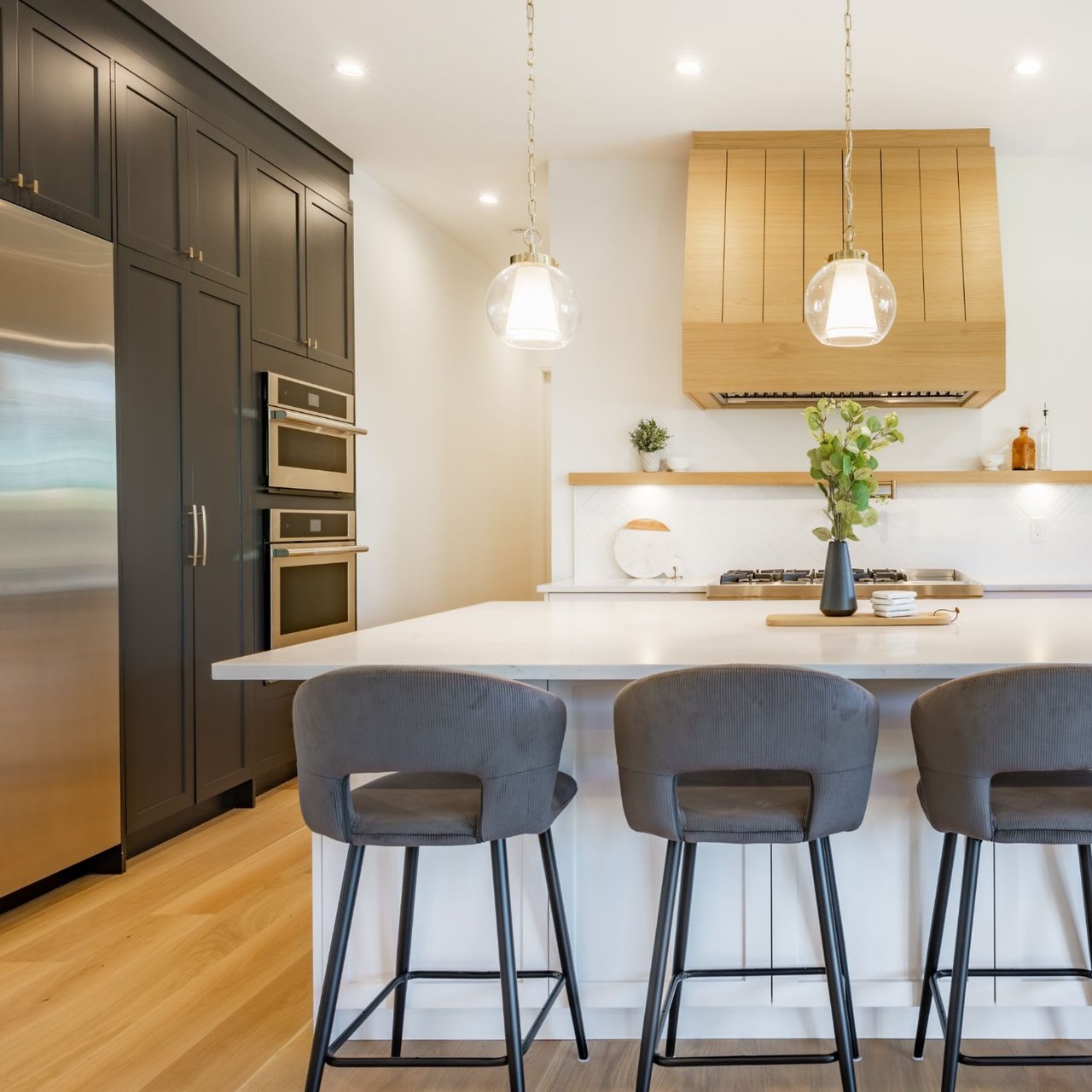  A modern kitchen features a large white island with three grey bar stools. 