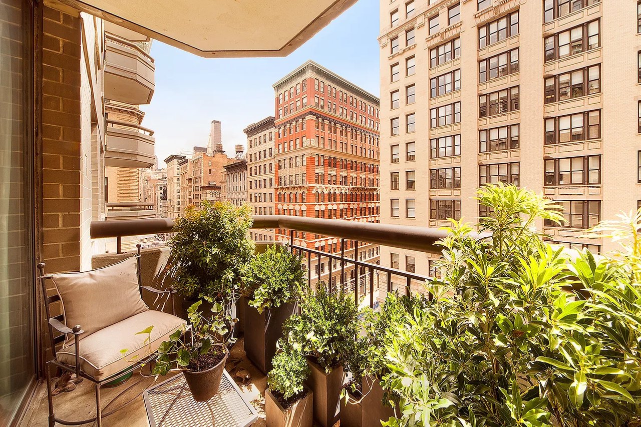 Apartment balcony with potted plants and seating overlooking neighboring city buildings.